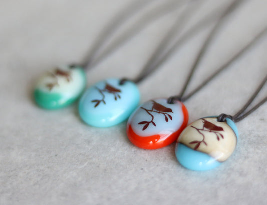 Four colorful glass necklaces with nature-themed designs on a light gray background
