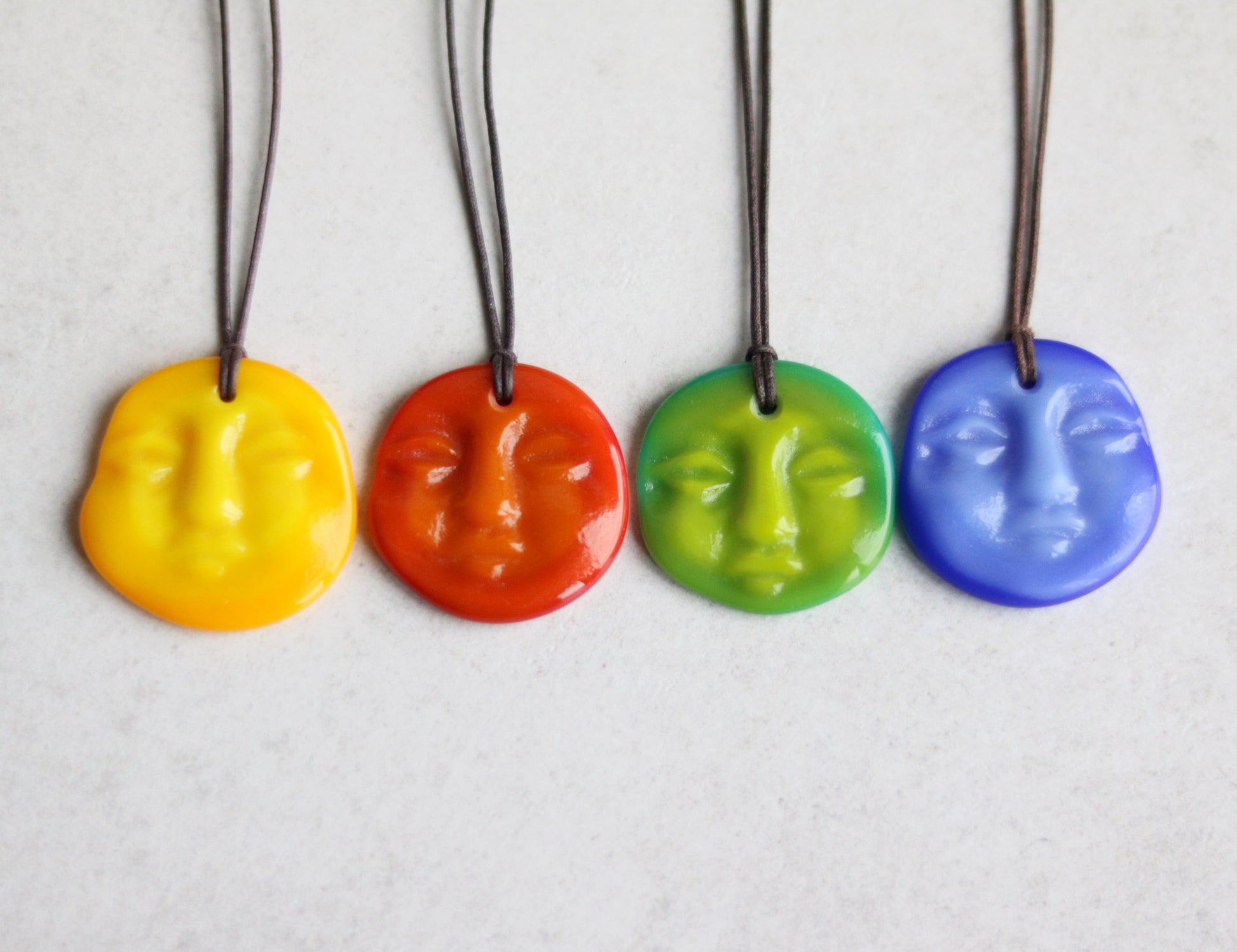 Four colorful face-shaped pendants on strings against a light background