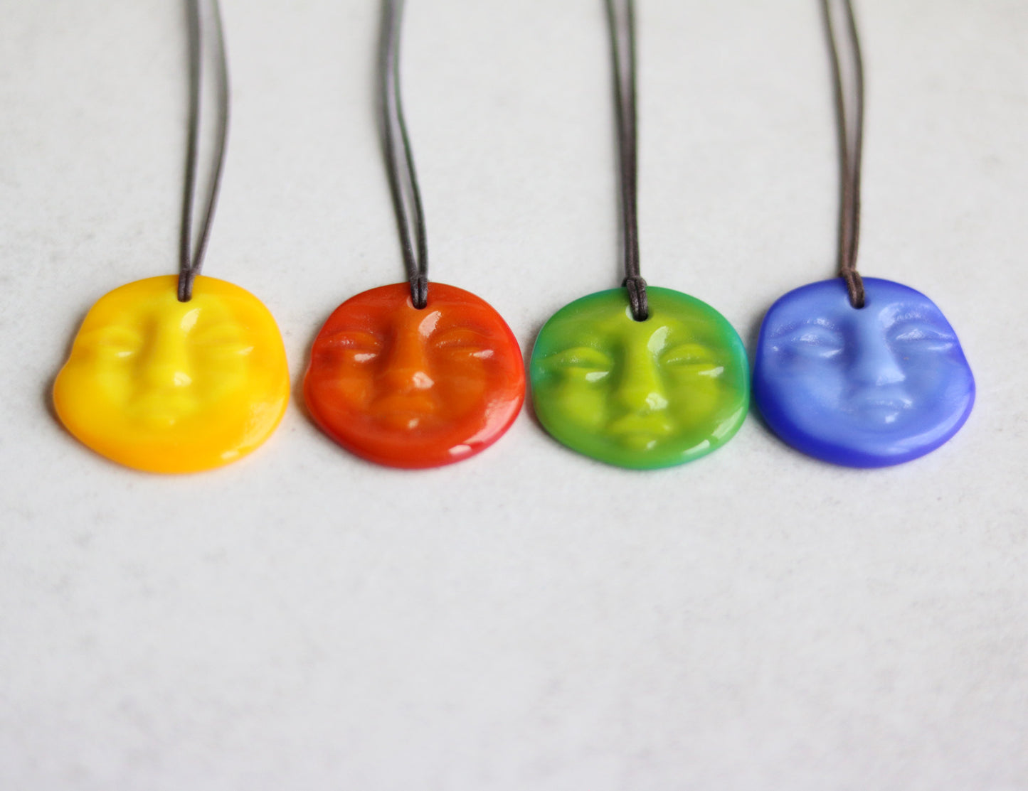Four colorful face-shaped pendants on strings against a light background