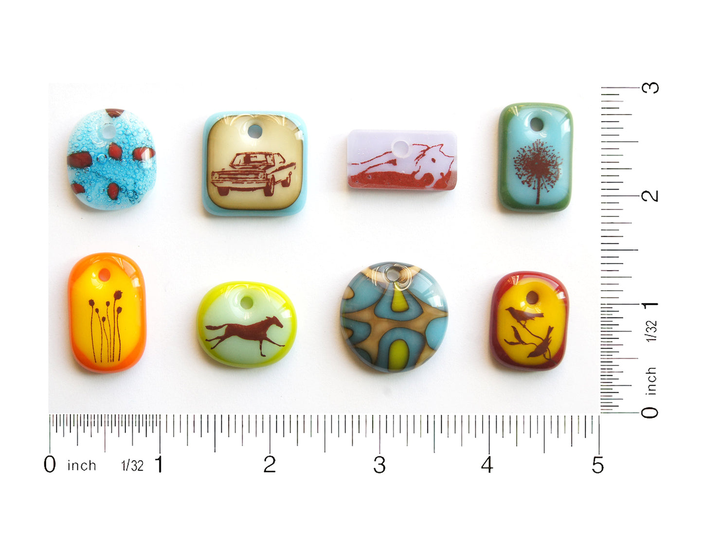Handmade glass pendants made by Leila Cools on a grid with ruler to show size.