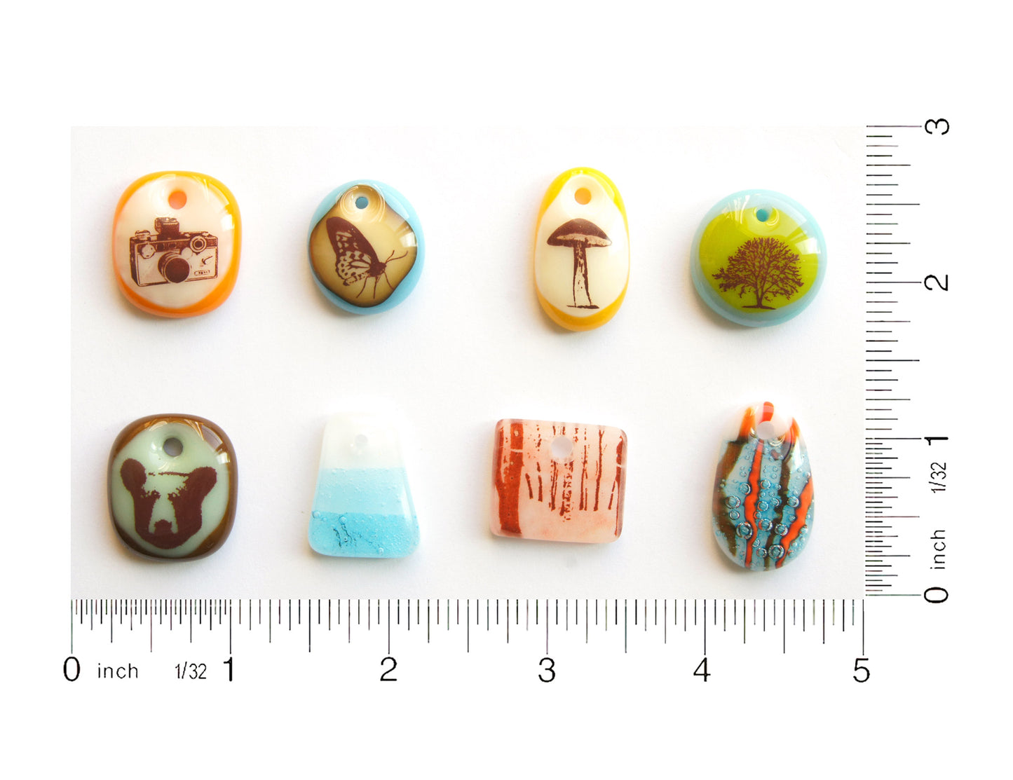 Eight glass pendants handmade by Leila Cools on a grid with ruler to show size.