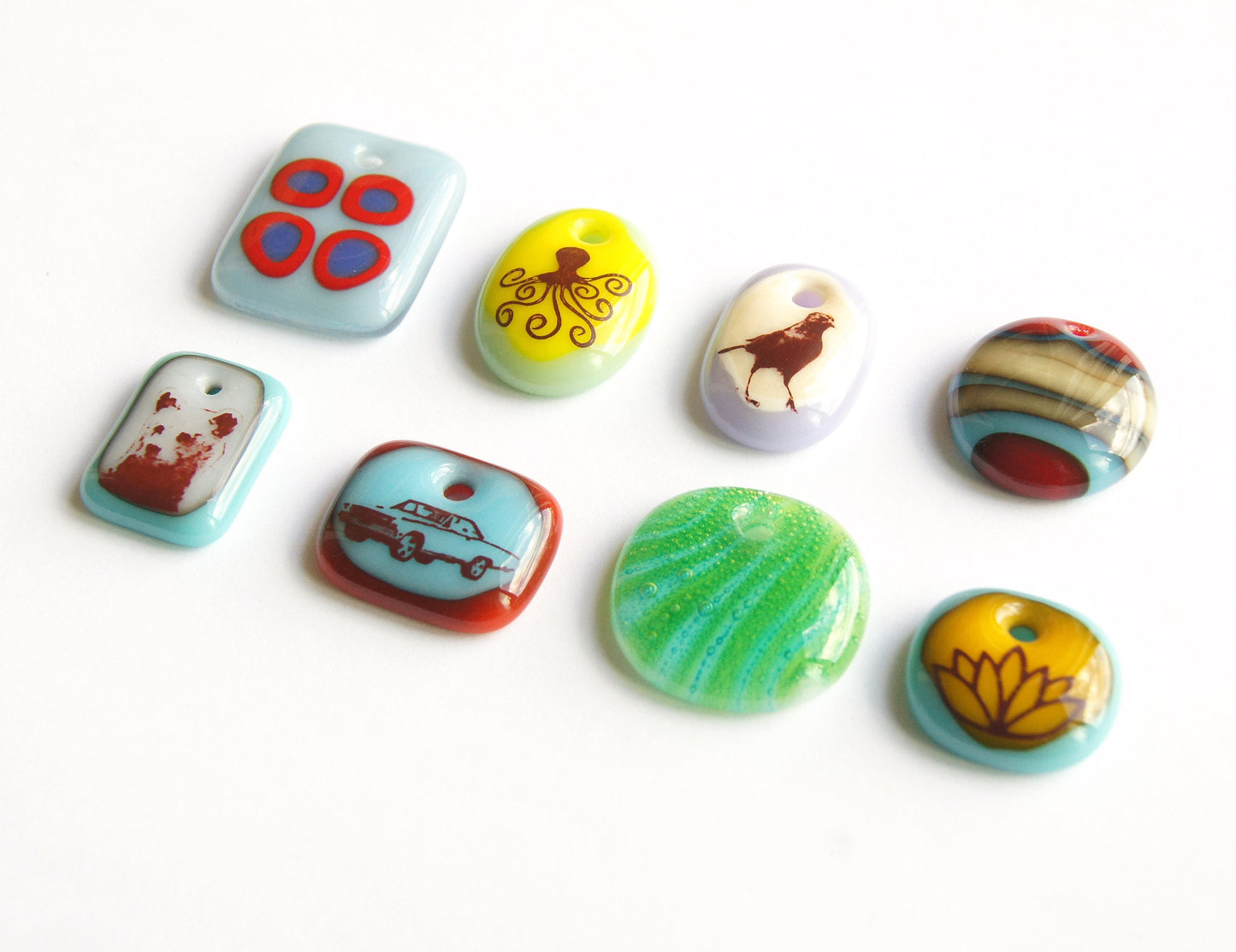 Eight handmade glass necklaces by Leila Cools in order, Red Circles on Blue, Octopus, Walking Bird, Vintage Stripes, Brown Bear, Vintage Car, Retro Green Stripes, Lotus Flower