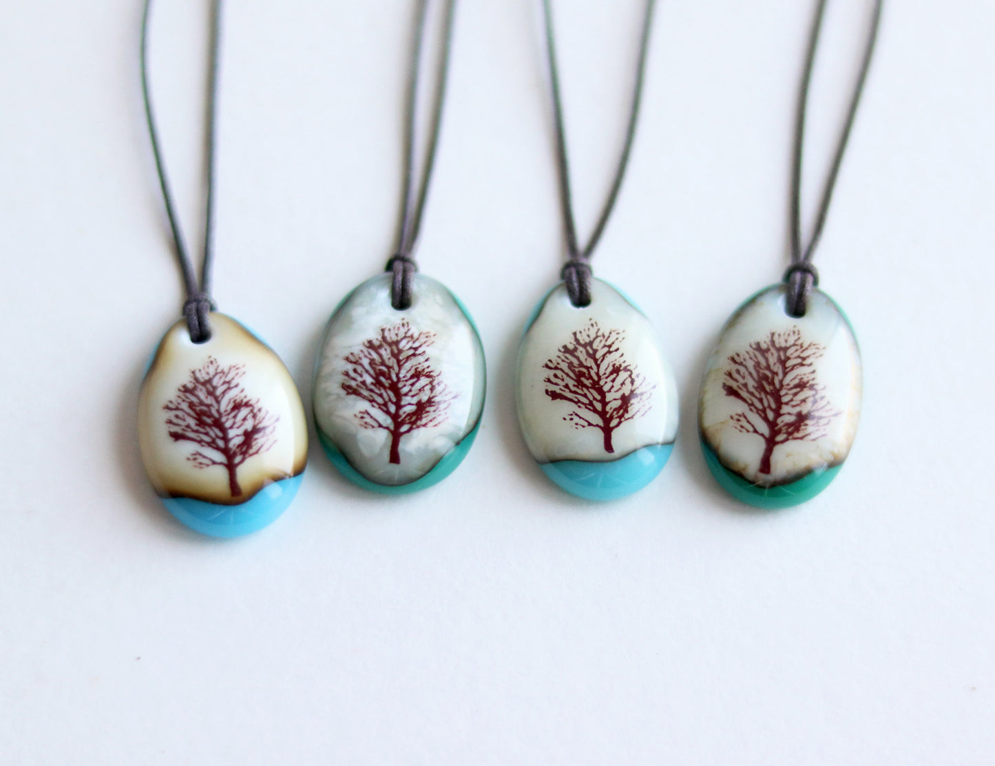 Four necklaces with tree designs on pendant stones against a white background