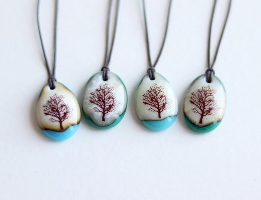 Four necklaces with tree designs on pendant stones against a white background