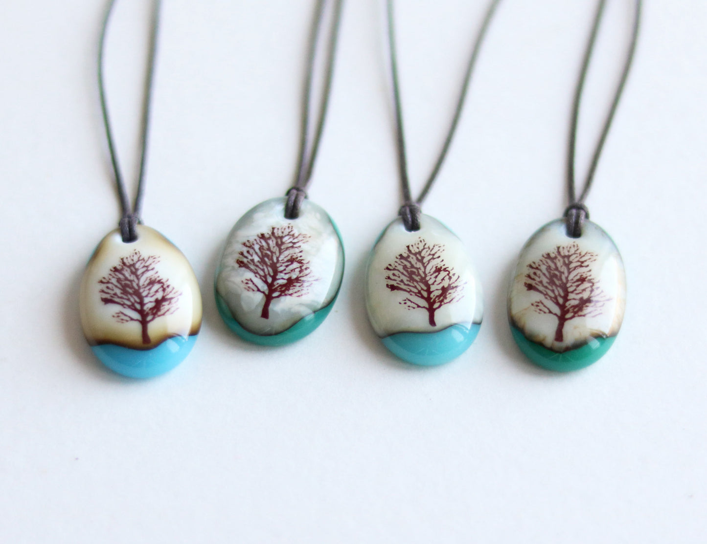Four necklaces with tree designs on oval pendants against a white background