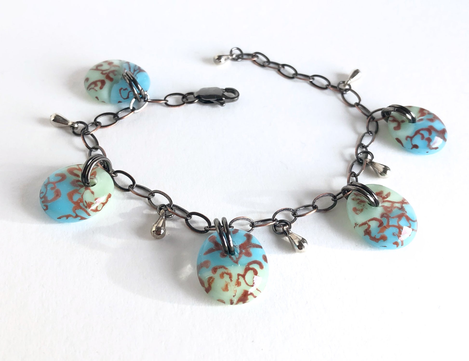 Charm bracelet with sepia tone filigree design on blue and green glass.