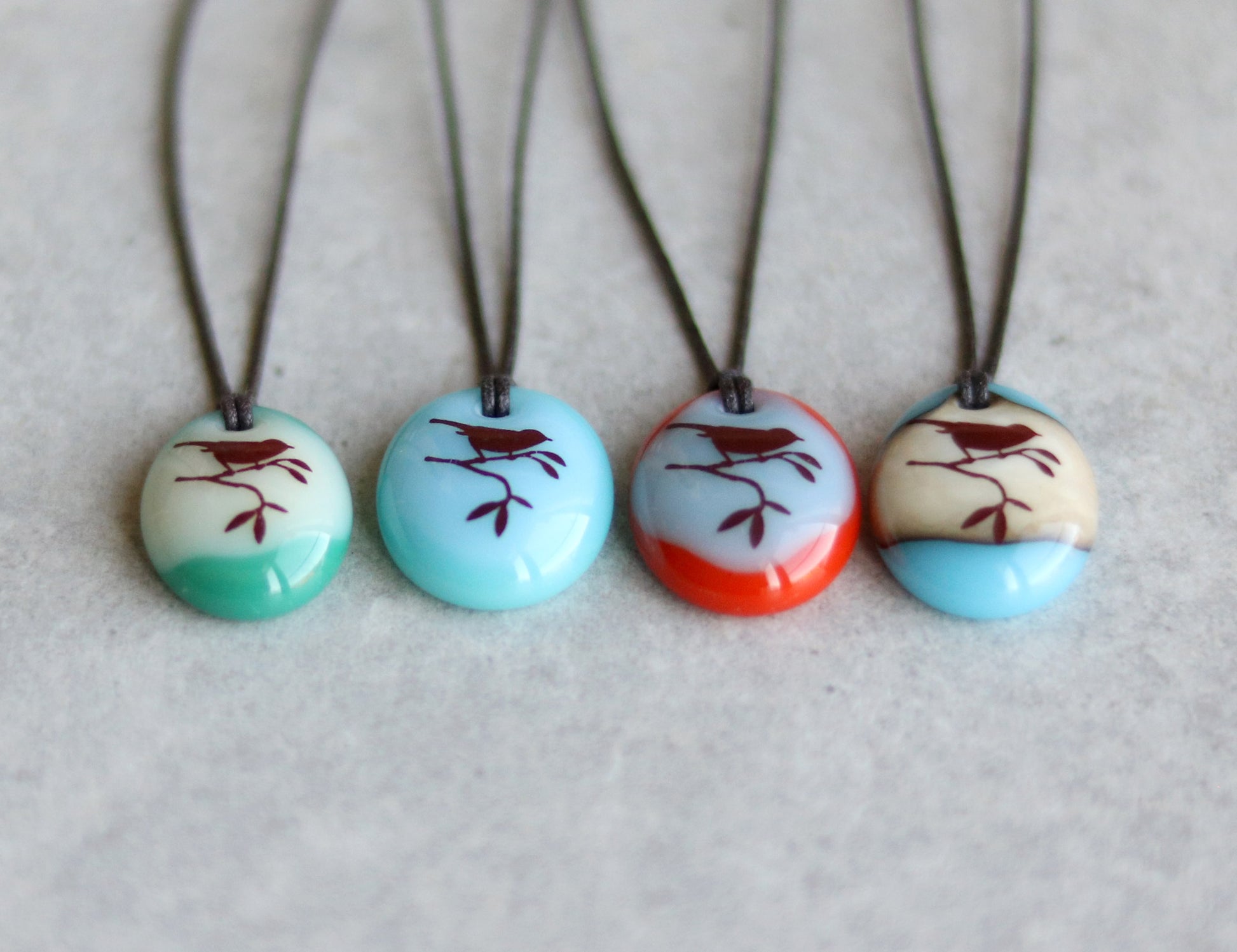Four necklaces with oval pendants featuring bird designs in various colours