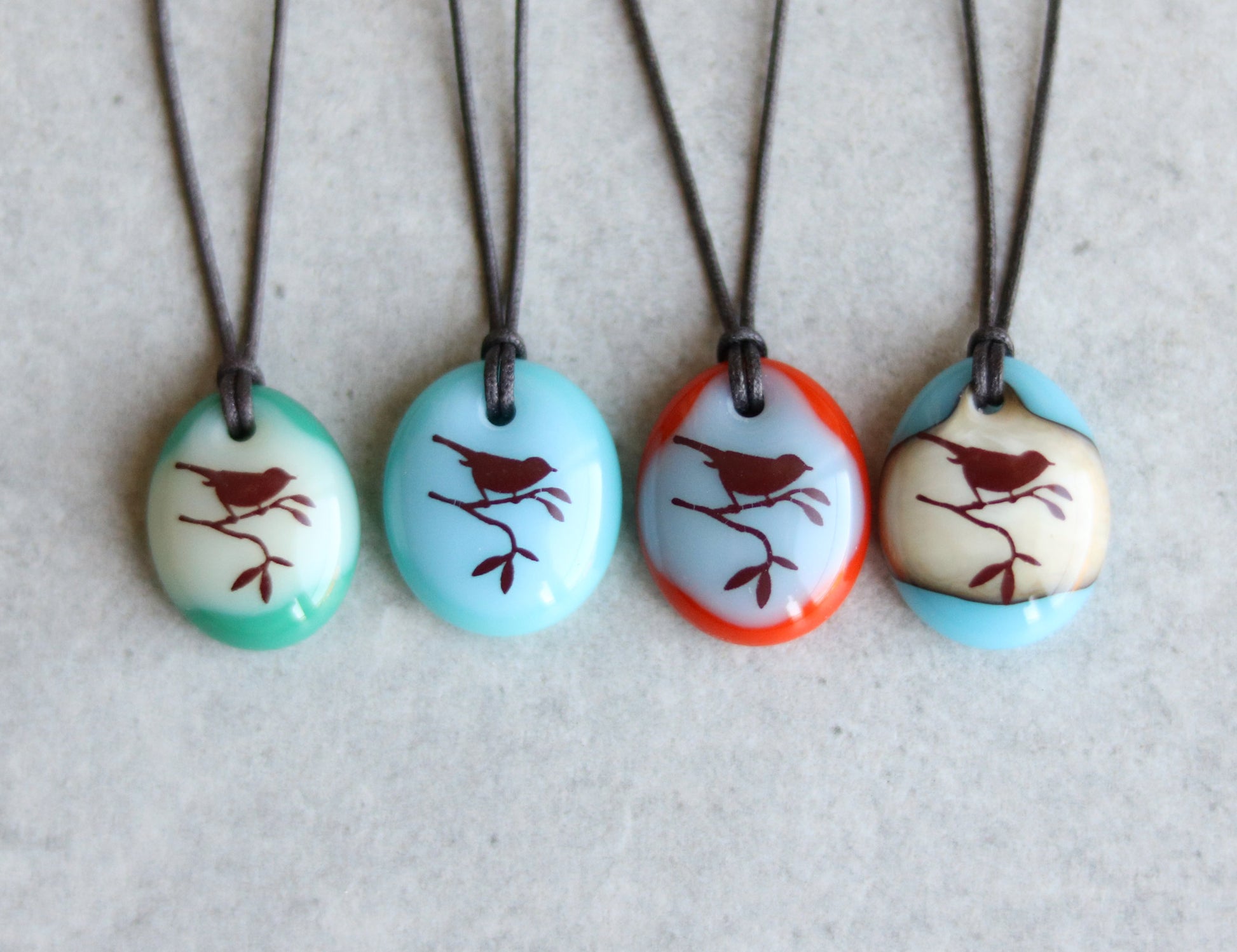 Four necklaces with oval pendants featuring bird designs on a light gray background