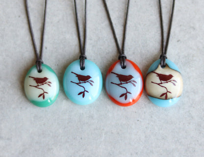 Four necklaces with oval pendants featuring bird designs on a light gray background