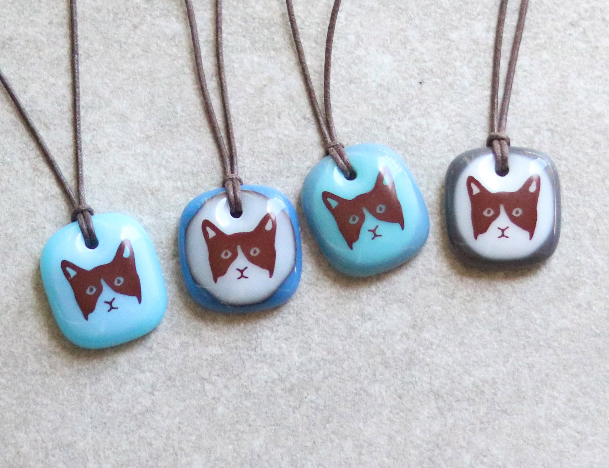 Assortment of four necklaces with glass pendants featuring cat illustrations on a neutral background