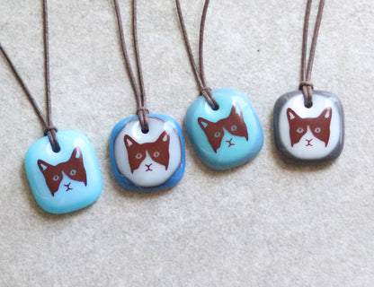 Assortment of four necklaces with glass pendants featuring cat illustrations on a neutral background