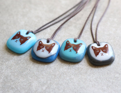 Four glass pendant necklaces with cat designs on a grey ceramic surface