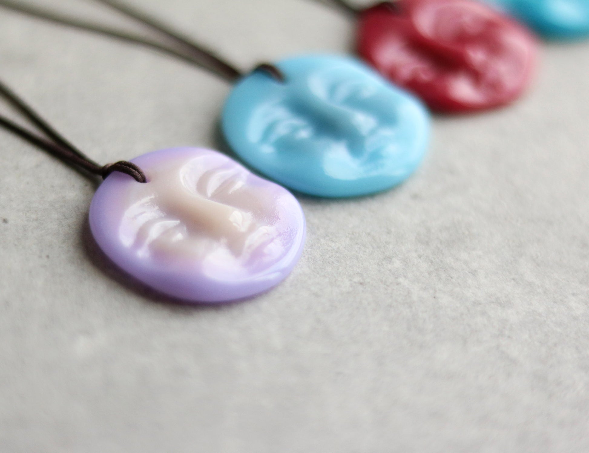Colorful glass disc necklaces in the shape of a serene face on a gray surface