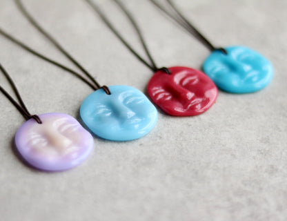 Four colorful necklaces with face-shaped pendants on a gray background