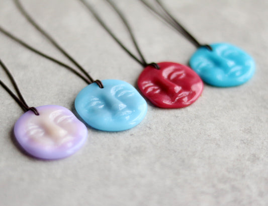 Four colorful necklaces with face-shaped pendants on a gray background