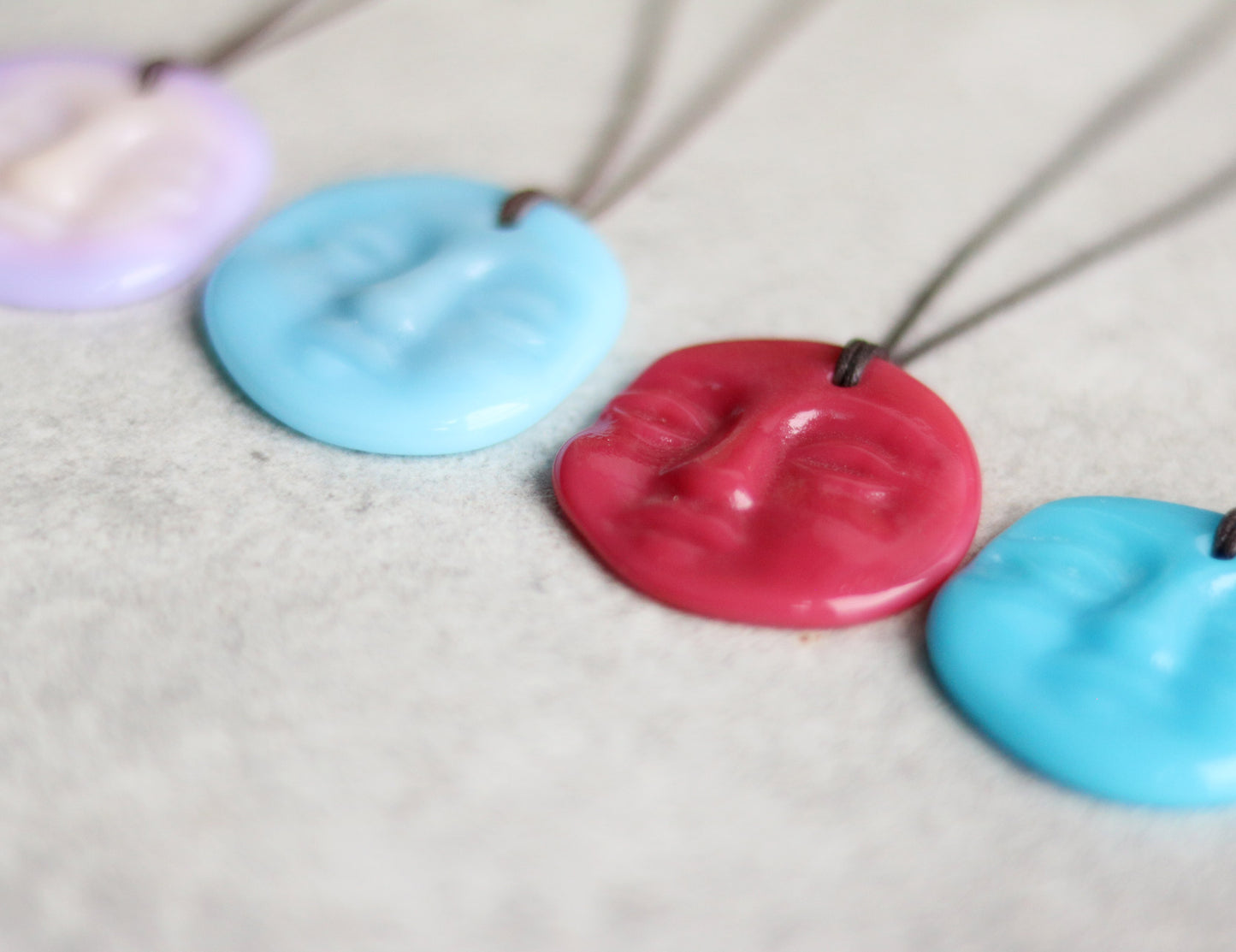 Aqua blue, purple, and pink handmade glass pendant necklaces on a textured surface