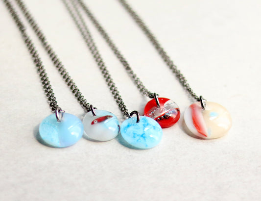 Four necklaces with colorful pendant designs on a light background