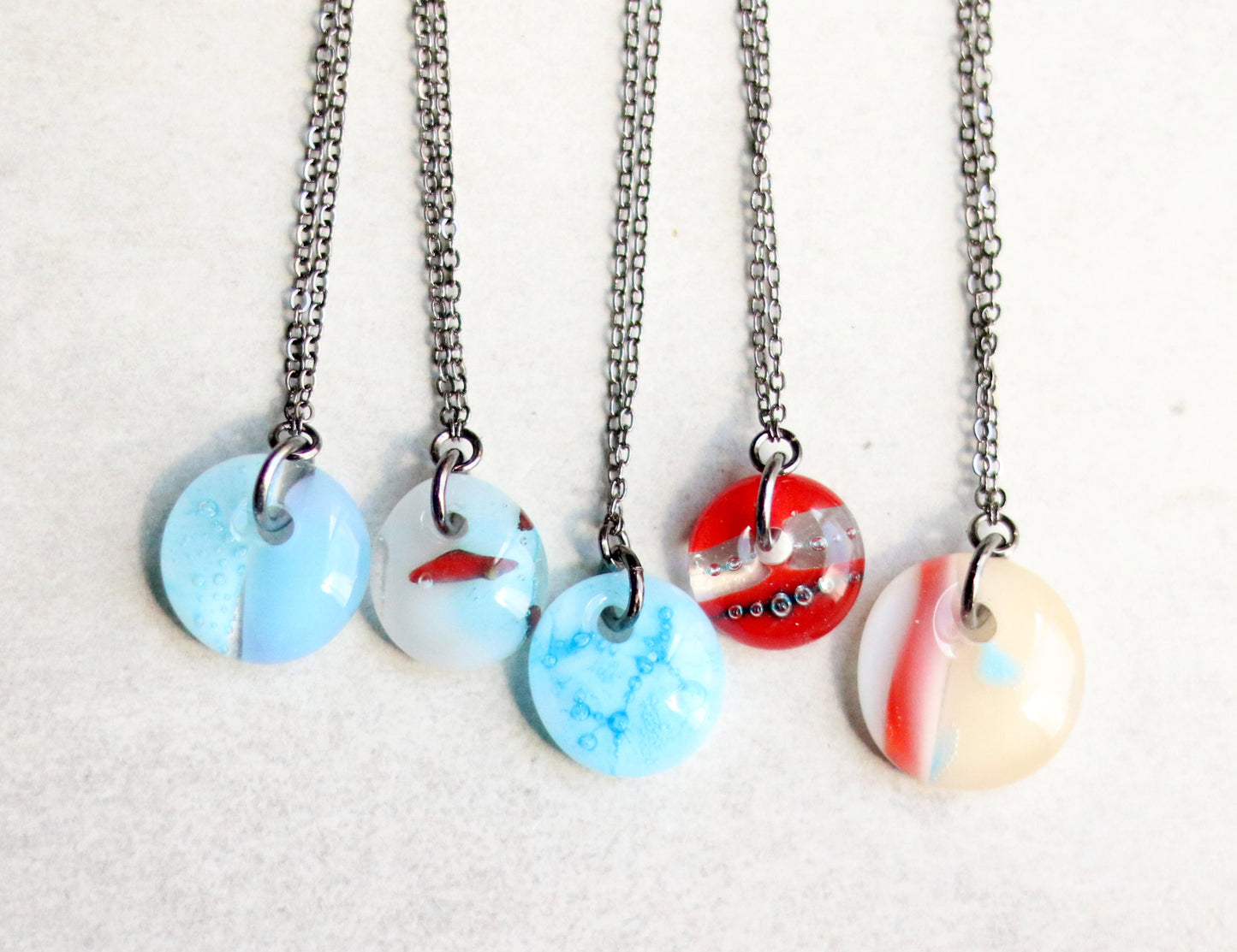 Five necklaces with round, multicolored pendants on a light gray background