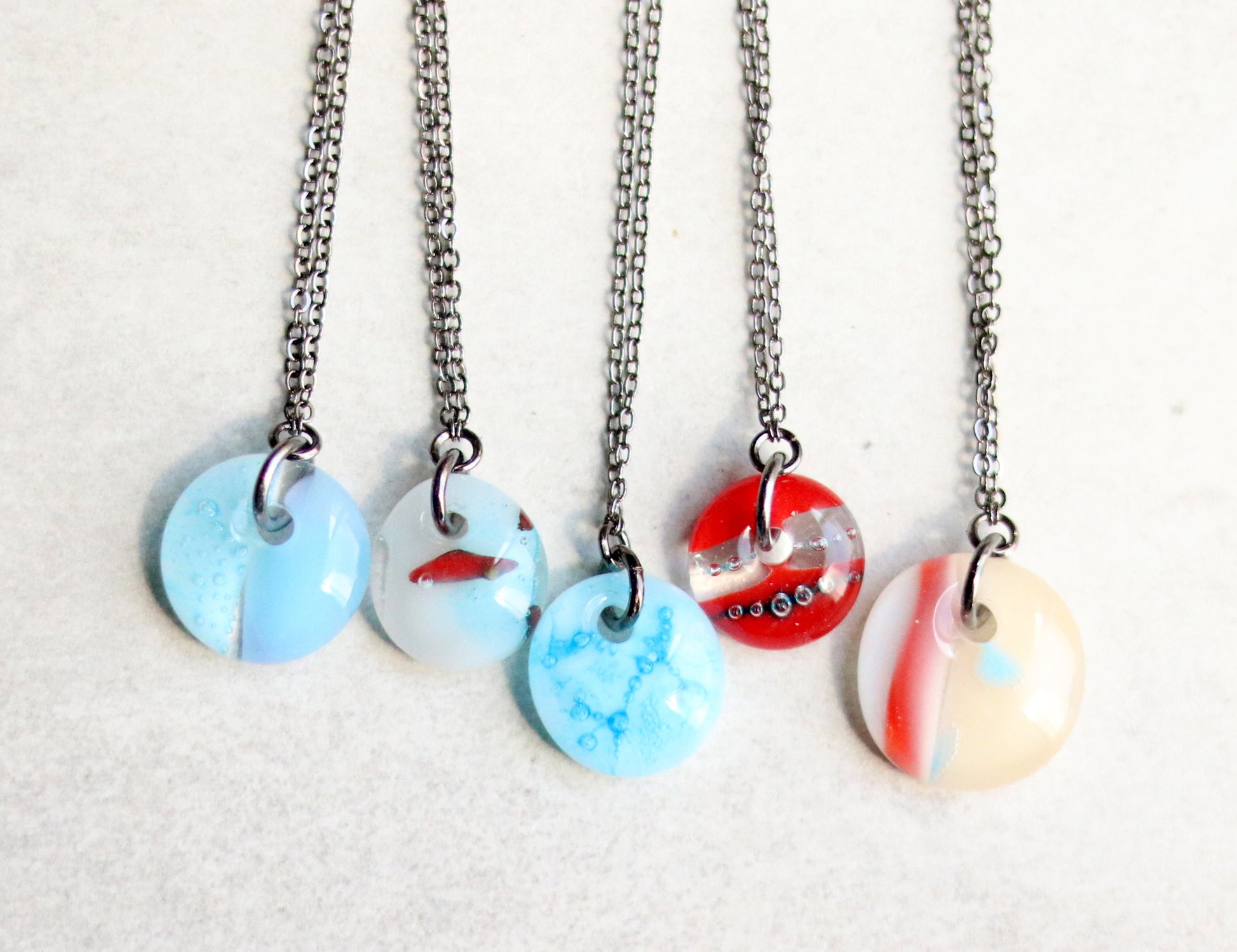 Five necklaces with round, multicolored pendants on a light gray background