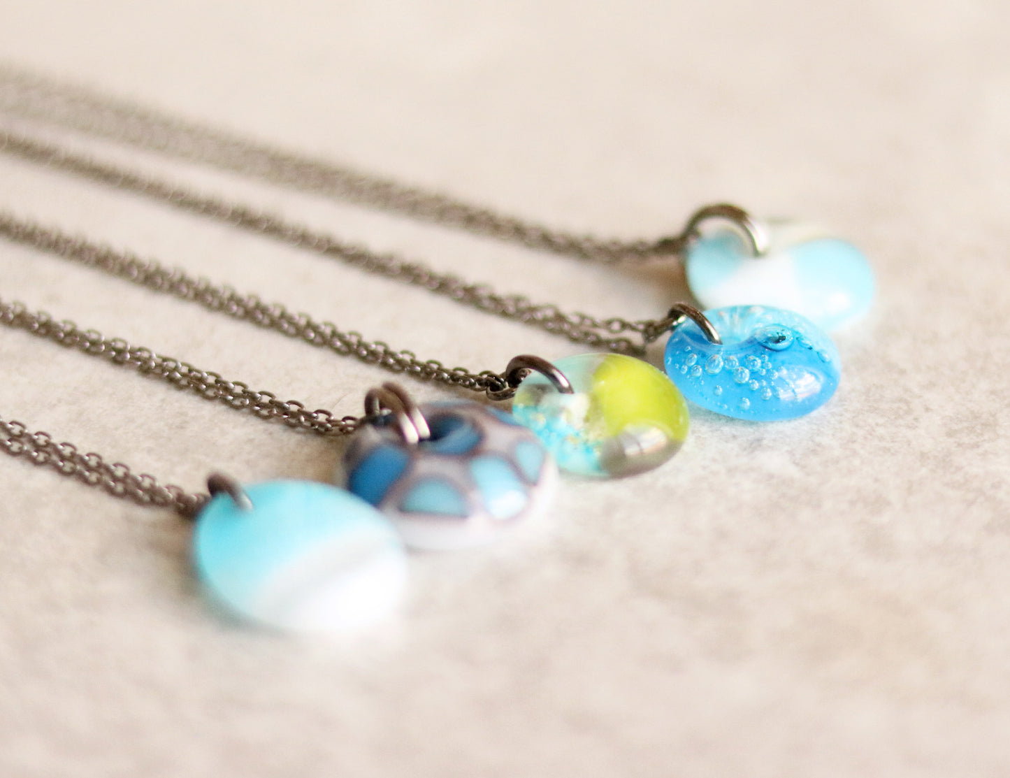 Five necklaces with colorful bead pendants on a beige background