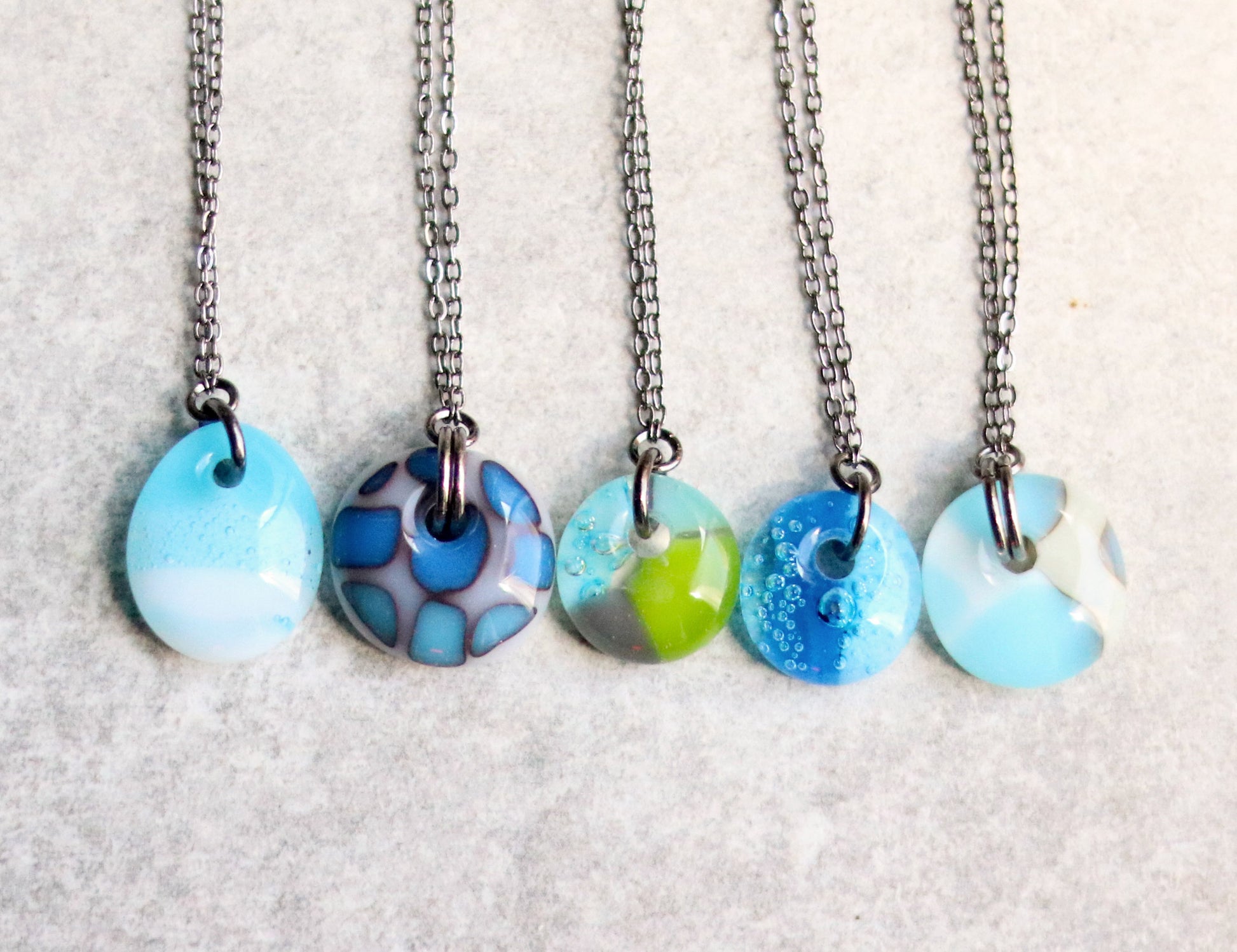 Five necklaces with colorful pendant designs on a light gray background