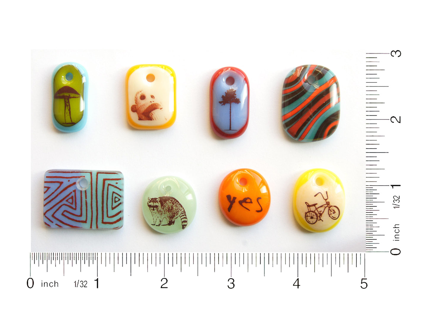 Eight handmade glass pendants on a grid with ruler to show size. 