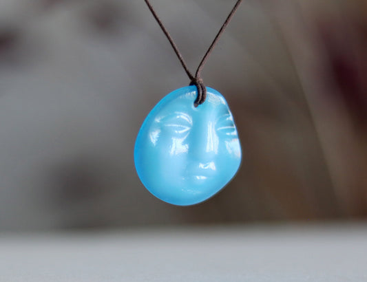 Blue pendant int the shapes of a face on a cord against a blurred background