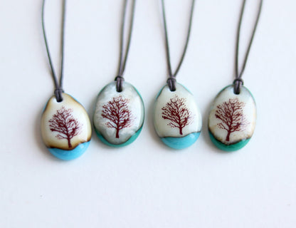 Four necklaces with tree designs on pendant stones against a white background