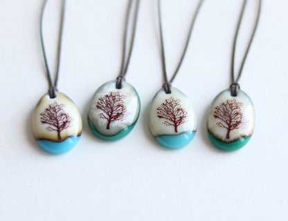 Four necklaces with tree designs on oval pendants against a white background