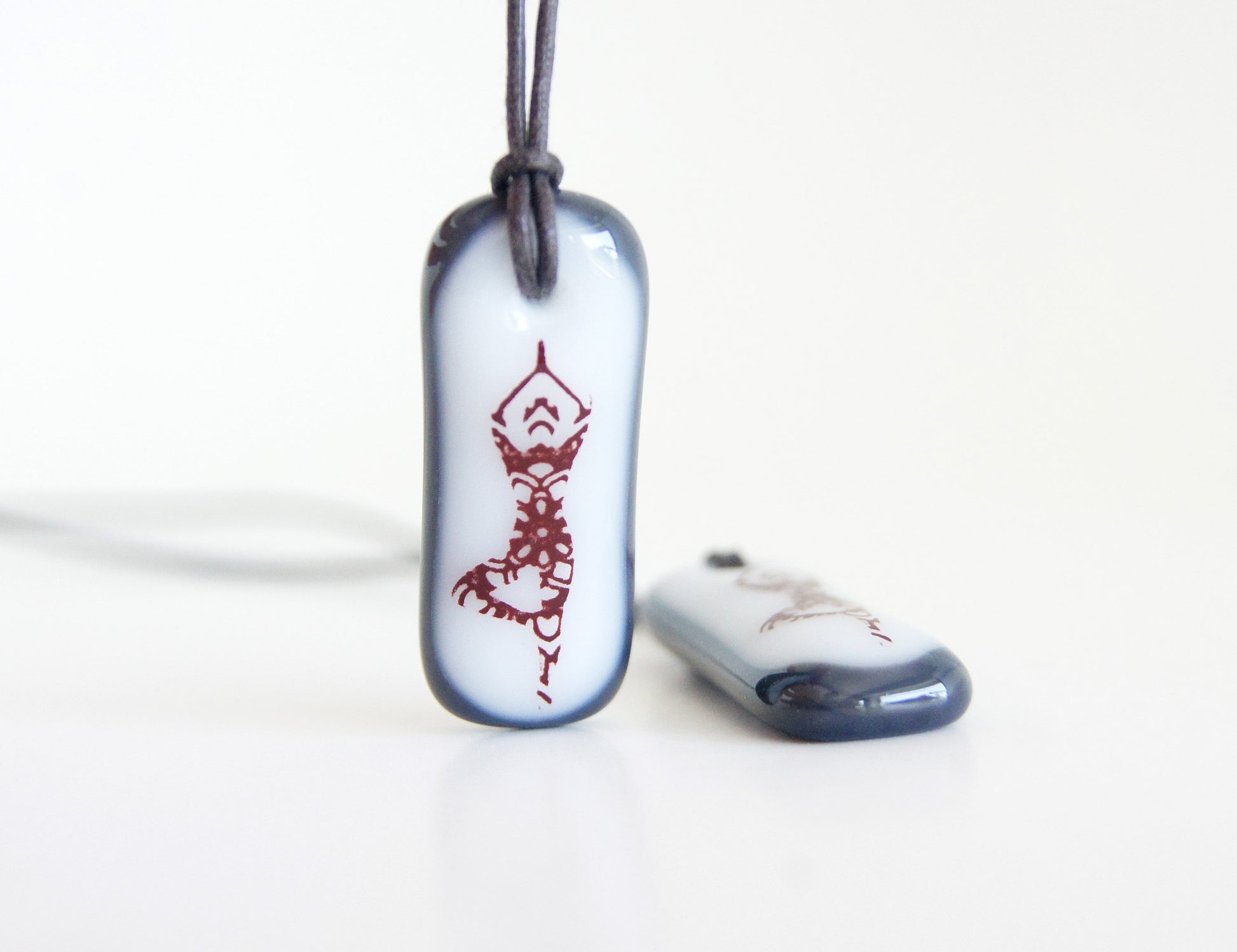 A fused glass white and dark grey pendant necklace with a yoga lover tree pose image.